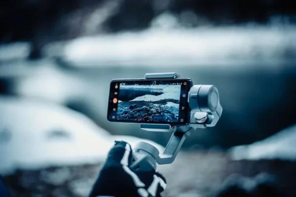 A smartphone mounted on a stabilizer capturing a snowy winter scene outdoors.